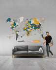 Man standing in a room with a large world map on the wall above a gray sofa.