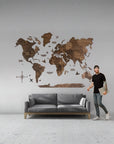 Man standing next to a large wooden 2XL size world map on a wall in a modern living room.