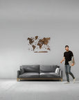 Man standing next to a gray sofa with a medium size wooden world map in a minimalistic room.