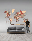 Man standing next to a 2XL size wooden world map on a gray wall with a gray sofa below.