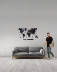 Man standing next to a gray sofa with a world map wall decal on a light gray wall.