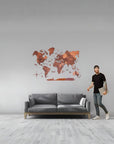 Man standing next to a gray sofa with a large size wooden world map in a room.