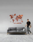 Man standing next to a gray sofa with a large size wooden world map in a room.