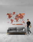 Man standing next to a gray sofa with a XL size wooden wall world map in a room.