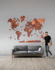 Man standing next to a gray sofa in a room with a 2XL size wooden world map on the wall.