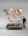 Man standing next to a 2XL size wooden world map on a gray wall with a gray sofa below.