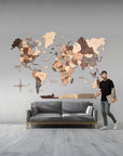 Man standing next to a 3XL size wooden world map on a gray wall with a gray sofa below.