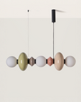 A modern multi-light linear pendant chandelier with glossy, rounded glass globes in muted pastel colors including sage green, terracotta, beige, and white, suspended from a black ceiling canopy against a minimalist beige and white two-tone background.