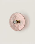 A pink colour textured glass wall light in shape of a disc on a light cream colour background