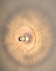A pink colour textured glass wall light lit up in shape of a disc on a light cream colour background
