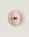 A pink colour textured glass wall light in shape of a disc on a light cream colour background