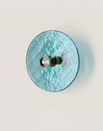 A blue colour textured glass wall light in shape of a disc on a light cream colour background