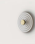 A round disc wall light on a light grey back ground.