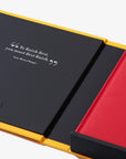 Two notebooks, one black with yellow edges and the other red with black edges, on a white background.