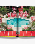 Luxury Poolside View in Miami Beach Book – Aerial shot of a stylish Miami Beach resort pool with red and white umbrellas, featured in the Assouline coffee table book. Find it at Spacio India.
