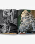 A grand, black-and-white staircase with ornate iron railings and intricate sculptures and a close-up of an ancient marble statue of a bearded man on a double spread in a luxurious Assouline Milan Chic coffee table book, showcasing Milan’s timeless elegance, now available at Spacio India’s online store and retail outlets.