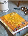 Assouline's Milan Chic coffee table book with a vibrant yellow cover, placed on a stylish glass table with wooden legs, accompanied by decorative items in a modern interior setting in a luxurious Assouline Milan Chic coffee table book, showcasing Milan’s timeless elegance, now available at Spacio India’s online store and retail outlets
