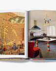 A vibrant interior spread featuring an artistic dining space with a golden mosaic wall and a colorful, modern kitchen with eclectic design elements on a double spread in a luxurious Assouline Milan Chic coffee table book, showcasing Milan’s timeless elegance, now available at Spacio India’s online store and retail outlets.