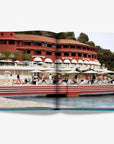 A seaside resort with red facade with waterfront terrace double spread in a luxurious Assouline's Monte Carlo coffee table book, featuring a vibrant cover with images of Monaco's iconic landmarks, available at Spacio India.