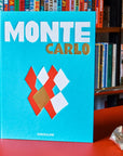 A bold turquoise Front cover in a Assouline's Monte Carlo coffee table book, featuring a vibrant cover with images of Monaco's iconic landmarks, available at Spacio India.