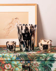 Artistic arrangement of Baobab Black Pearls Candle Max 10 with other sizes on vibrant tropical patterned surface, bringing luxurious fragrance to interiors. Buy at Spacio India.