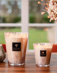 Pair of lit Baobab White Pearls candles in a cosy setting, showcasing luxurious floral ambiance, offered at Spacio India.