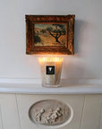 Candle on a white surface with a framed painting above it
