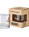 Clear glass shot glass with bullet design next to its packaging box on a white background