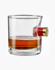 Glass filled with whiskey in a glass with shotgun shell casing, on a white background