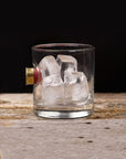 Clear glass with ice cubes and a bullet casing on a wooden surface