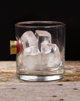 Clear glass with ice cubes and a bullet casing on a wooden surface