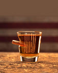 Shot glass with American flag design filled with a dark liquid on a wooden surface.