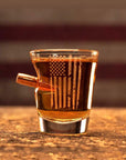 Shot glass with American flag design filled with a dark liquid on a wooden surface.
