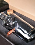 Glass whiskey decanter with a bullet inside, placed in a cardboard box.