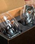 Two clear wine glass with bullets shot in the glass in a cardboard box with foam padding.