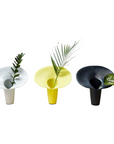 Three modern vases in white, yellow, and black with plant leaves on a white background