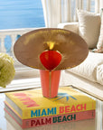 Decorative table lamp with a gold and red design on top of books titled 'Miami Beach' and 'Palm Beach' in a living room setting.