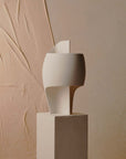 White table lamp on a beige pedestal against a textured beige wall