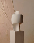 White table lamp on a beige pedestal against a textured beige wall