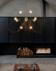 Modern chandelier hanging above a fireplace with firewood and a small table with items.