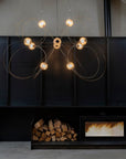 Modern chandelier hanging above a fireplace with firewood and a small table with items.