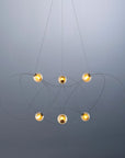 Modern chandelier with six hanging lights on a gray background from DCW Editions
