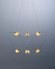 Modern chandelier with six hanging lights on a gray background from DCW Editions
