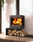 A modern black wood-burning fireplace with an open fire visible inside, set on a black hearth with stacked firewood logs. The stove has a vertical chimney pipe extending upwards.
