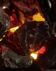 Close-up of dark, irregularly shaped glass or crystal pieces glowing with red and orange light, filling the frame in a gas fireplace