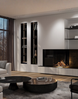 A modern living room interior with a white sofa, round coffee tables, a black leather chair, a gray rug, built-in shelving, and a gas fireplace with logs burning. No people or animals are present.