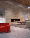 A modern living room interior with a large red armchair in the foreground, a light gray sofa, a low round coffee table, a shag rug, and a built-in linear gas fireplace set into a wood-paneled wall.