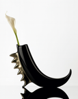 Black and gold vase with a white flower on a light gray background