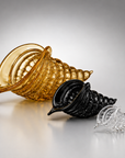 Three sculptural crystal conical vessels with textured bubble patterns, shown in amber, black, and clear glass on a reflective gray surface.