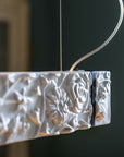 Decorative white ceramic suspension lamp with floral patterns hanging against a dark background
